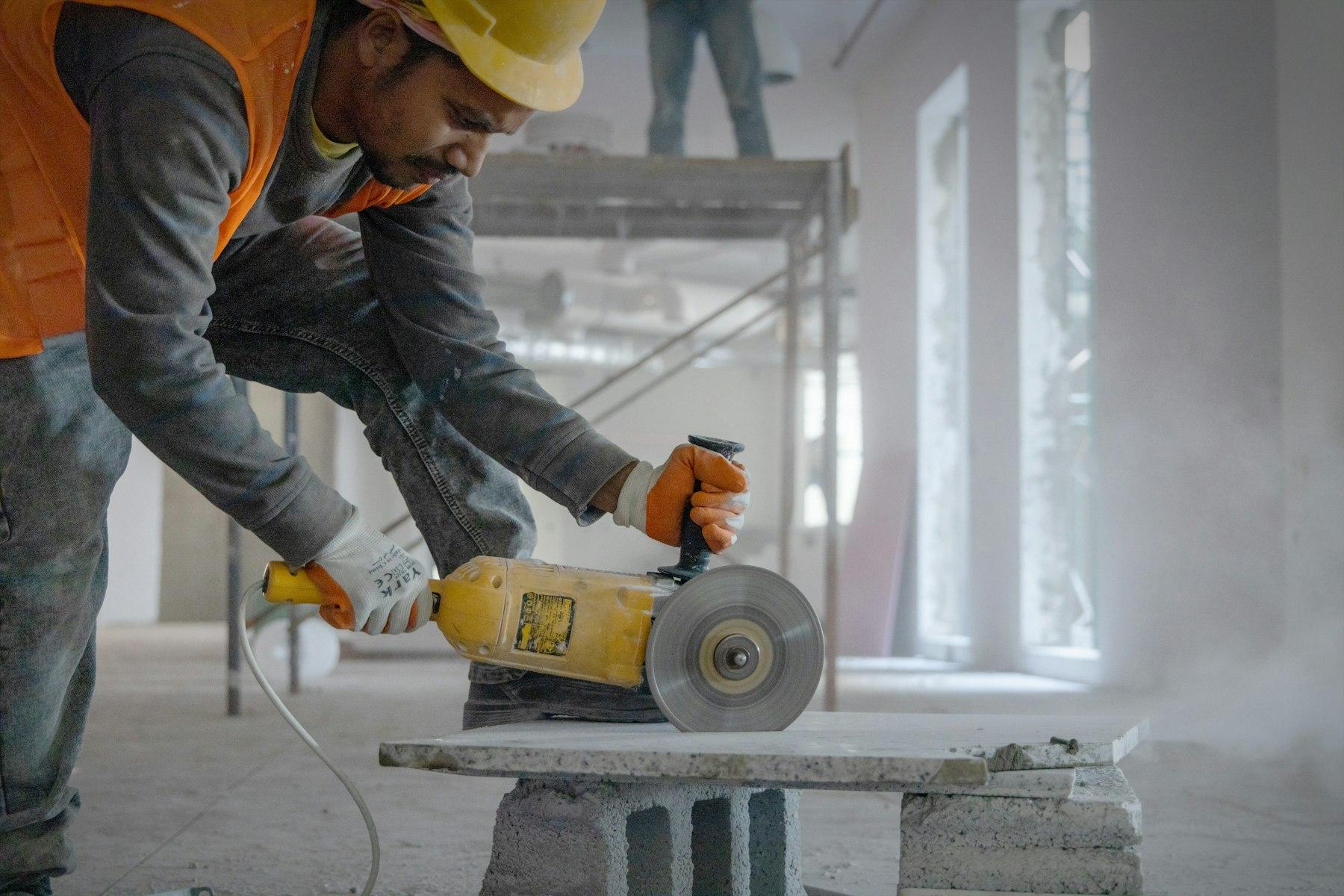 A tradesman in a hard hat cutting concrete with an angle grinder